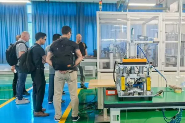 A group of men are gathered in a factory, observing a piece of machinery.