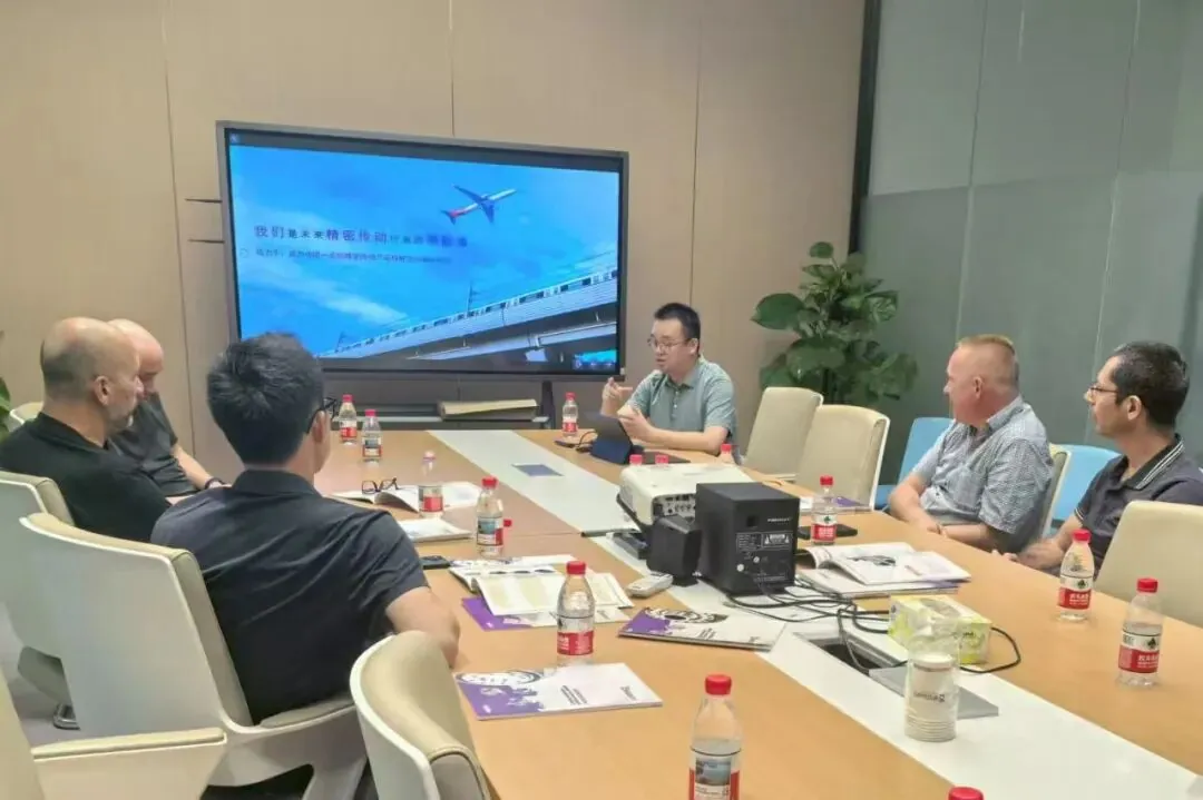 A man gestures while speaking to a group of men seated around a conference table.