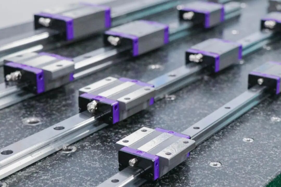 Multiple linear guide rails with silver blocks accented in purple mounted on a dark, speckled surface.