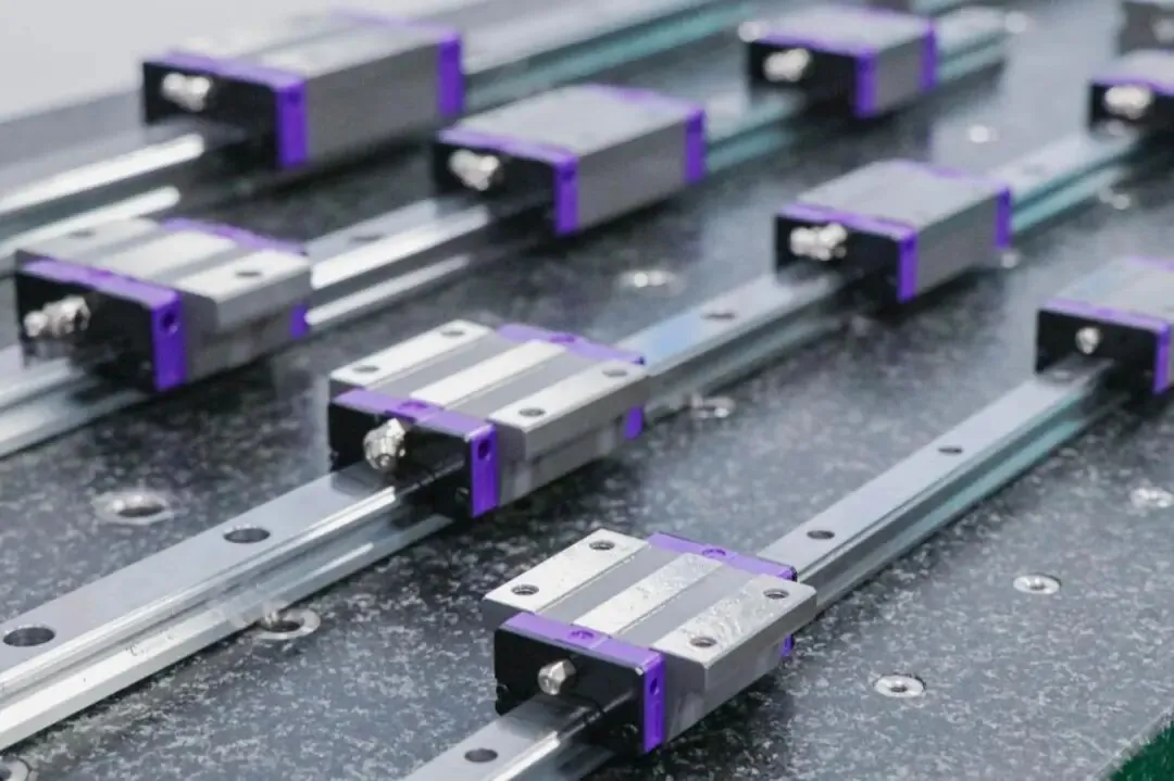 Multiple linear guide rails with silver blocks accented in purple mounted on a dark, speckled surface.