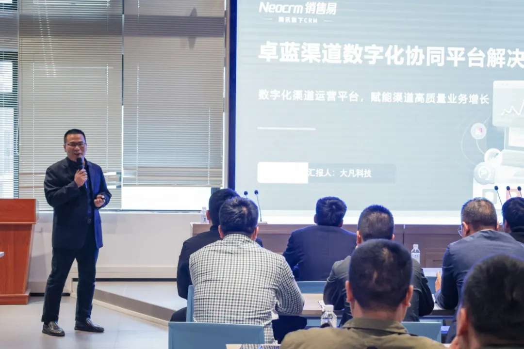 A speaker addresses an audience seated facing a presentation screen showing text.