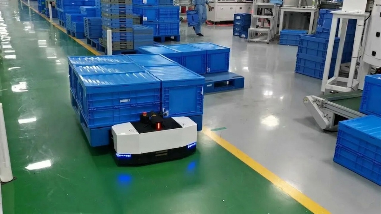 Autonomous Mobile Robot (AMR) transporting stacked blue plastic crates on a pallet in a clean industrial factory floor