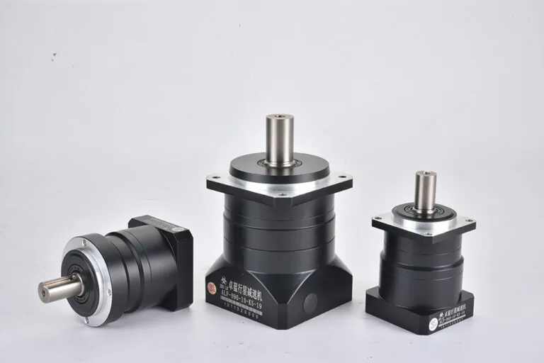 Three black planetary gearboxes of varying sizes are displayed on a white surface. The largest and smallest are upright, while the medium-sized one lies on its side. Each gearbox features a silver mounting flange and a polished output shaft. The largest gearbox has a label that reads "ALF-090-10-K5-19 1011320005". The smallest gearbox has a label that reads "ALF-060-10-K5-19 1011320001".