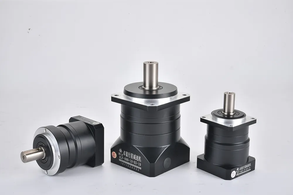 Three black planetary gearboxes of varying sizes are displayed on a white surface. The largest and smallest are upright, while the medium-sized one lies on its side. Each gearbox features a silver mounting flange and a polished output shaft. The largest gearbox has a label that reads "ALF-090-10-K5-19 1011320005". The smallest gearbox has a label that reads "ALF-060-10-K5-19 1011320001".