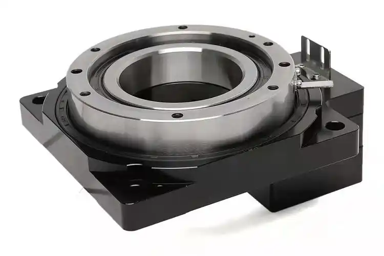 A black industrial rotary table with a large silver bearing in the center, featuring multiple bolt holes and a small metal lever on the right side.