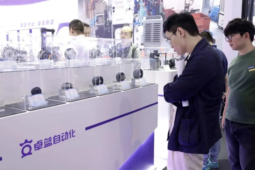 Two attendees examining precision mechanical components joint reducer displayed in acrylic cases at a trade show booth featuring the Zhuolan Automation logo.