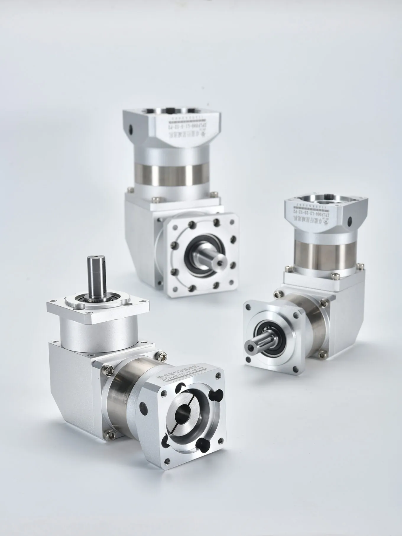 Three silver and gray right-angle planetary gearboxes on a white surface. The front gearbox has a vertical output shaft, while the two in the background have horizontal output shafts. Labels include "ZPLF060-L2-20-S2-P2" and "ZPLF090-L1-5-S2-P2".