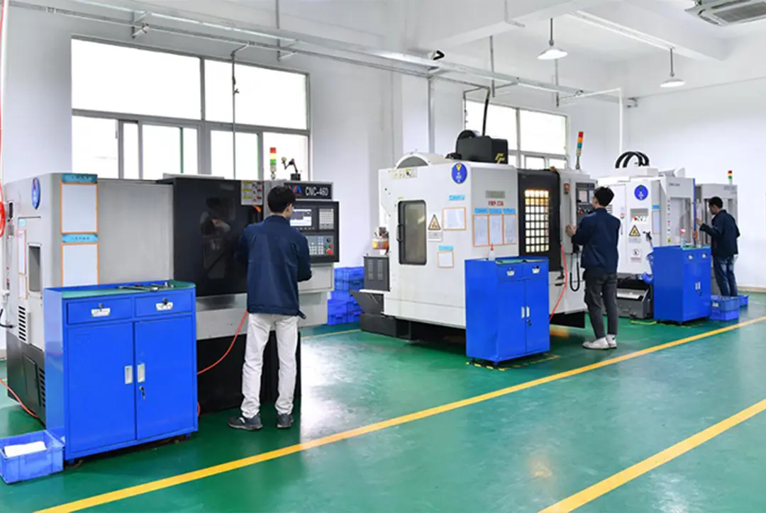 Workers operating CNC-460 and VMP-25A machines in a clean, well-lit factory with green floors and yellow safety lines. Blue tool cabinets are placed near each machine.