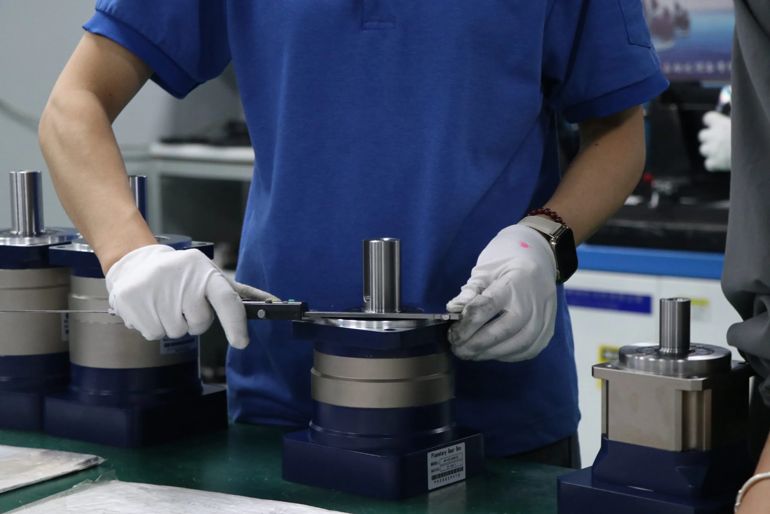 Close-up shot: A worker wearing white gloves is using a digital caliper to measure a planetary gearbox.