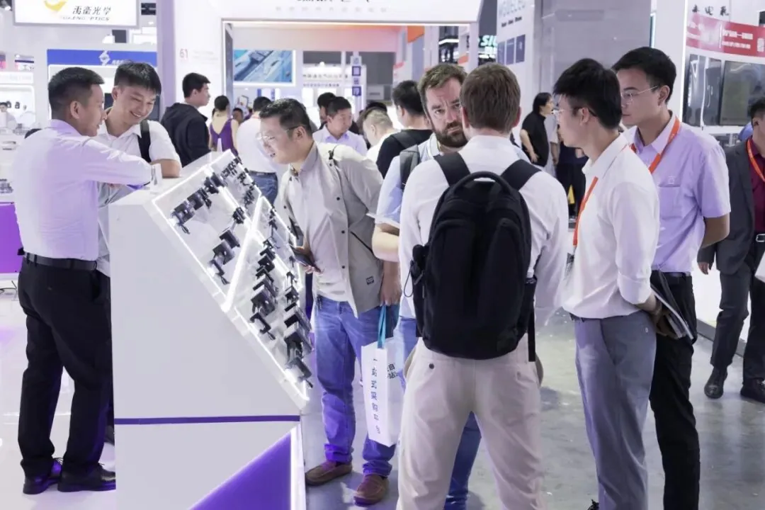 Overseas visitors examining precision linear guide rail samples displayed on angled shelves at a trade show booth.