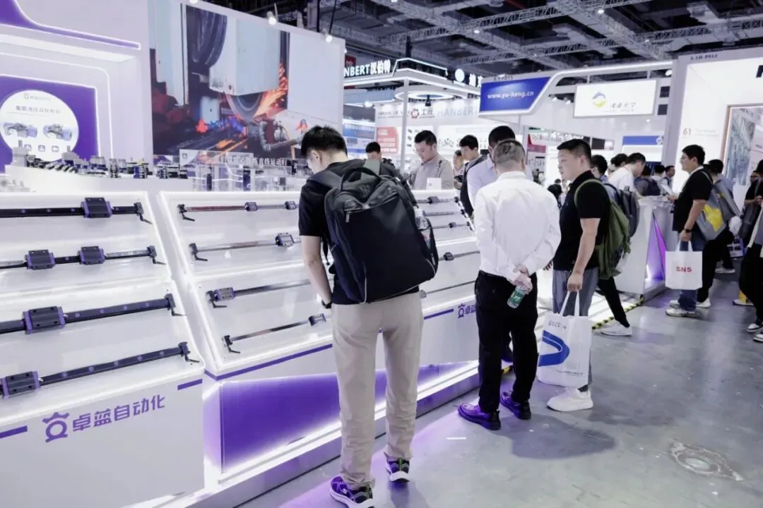 Visitors examining precision linear guide rail samples displayed on angled shelves at a trade show booth.