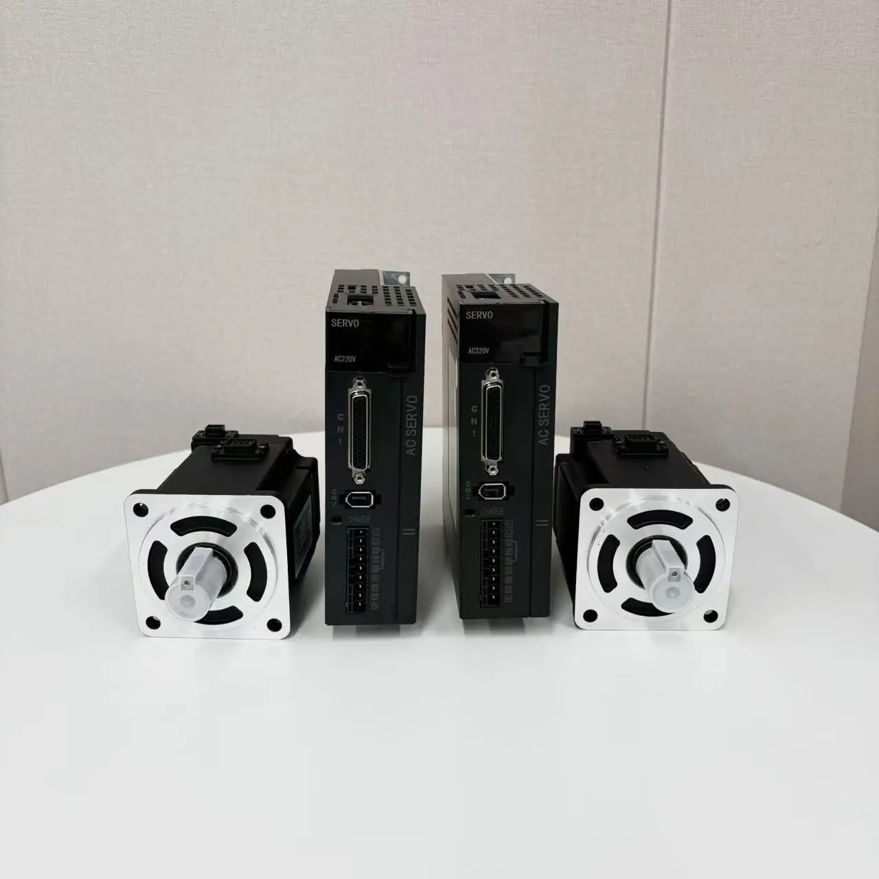 Two black servo drives labeled "SERVO AC220V AC SERVO" stand between two black stepper motors with silver faceplates and gray shaft covers, all on a white table.