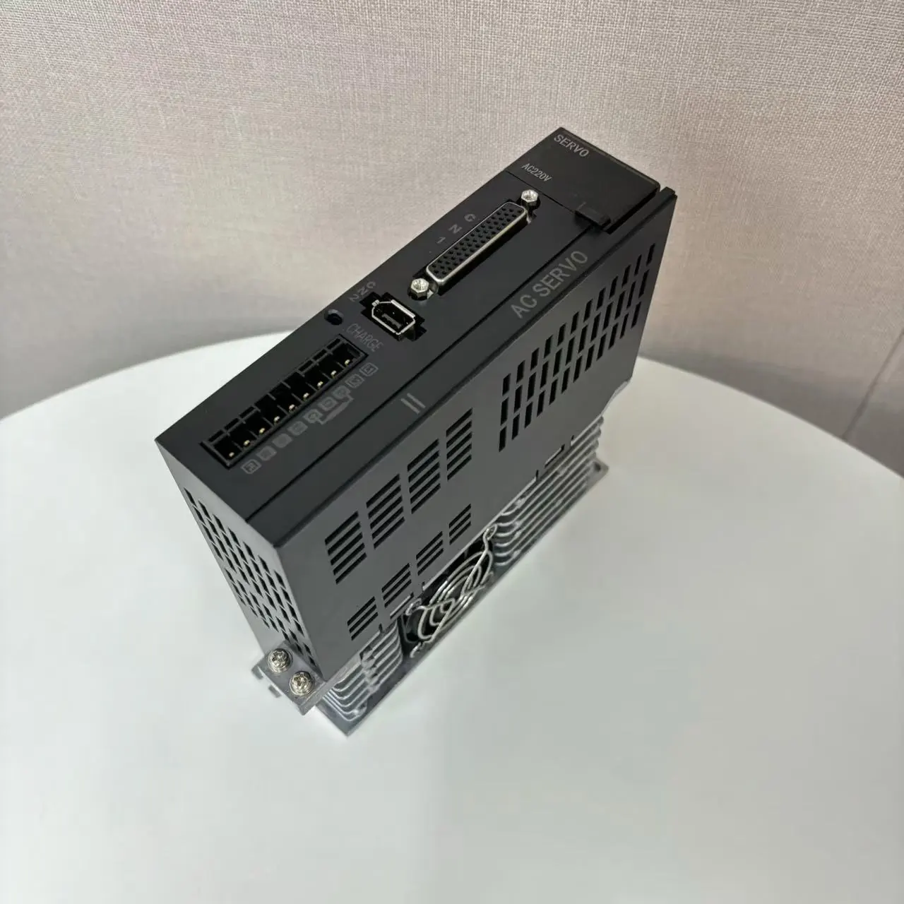 A black servo drive, labeled "SERVO AC220V AC SERVO," sits on a white table, angled to show its top and right side. It features a D-sub connector, a USB port, and a row of terminal blocks.