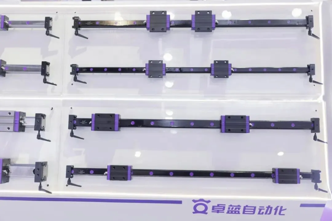 Precision linear guide rail samples with black rails and purple carriages displayed horizontally on a white exhibition rack.