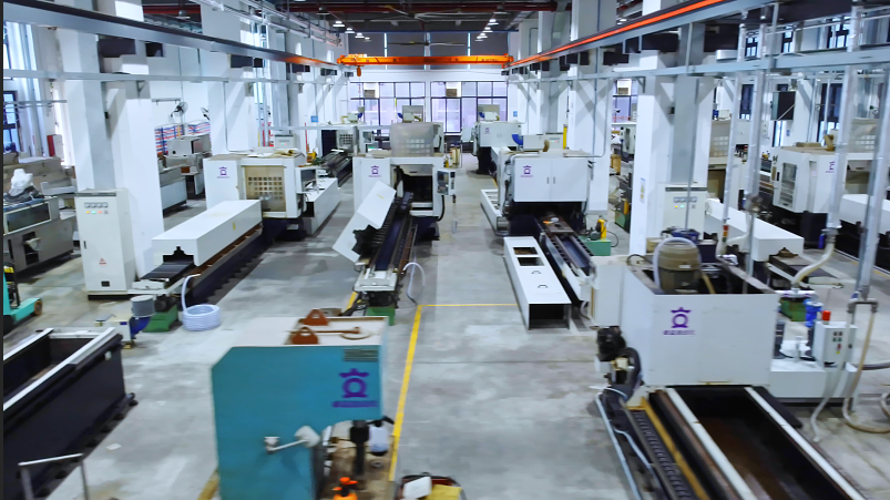 An aerial view of a spacious, well-lit factory floor with multiple white and teal industrial machines, some with the "QI" logo, arranged in rows.