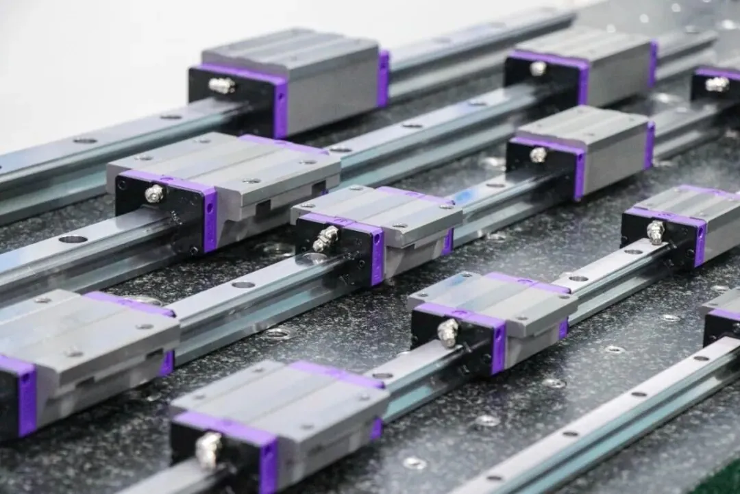 Close-up of multiple linear guide rails with carriages, featuring purple accents, arranged on a dark, textured surface.