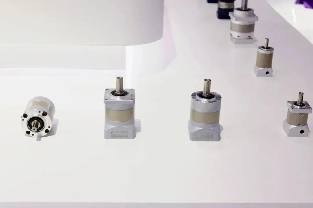 Several silver planetary gear reducers with output shafts displayed in a row on a white table.