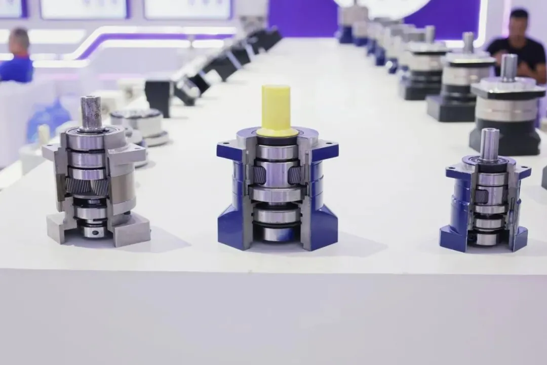Cutaway planetary gearboxes displaying internal gears and bearings in a row on a white exhibition table.