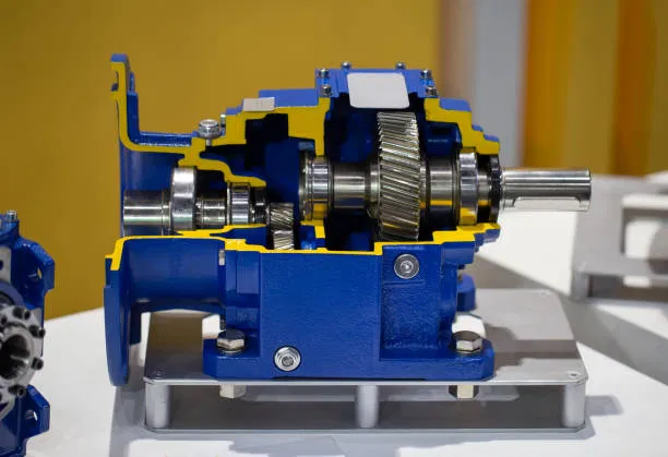 A cross-section cutaway view of a blue gearbox showing internal helical gears, shafts, and bearings.
