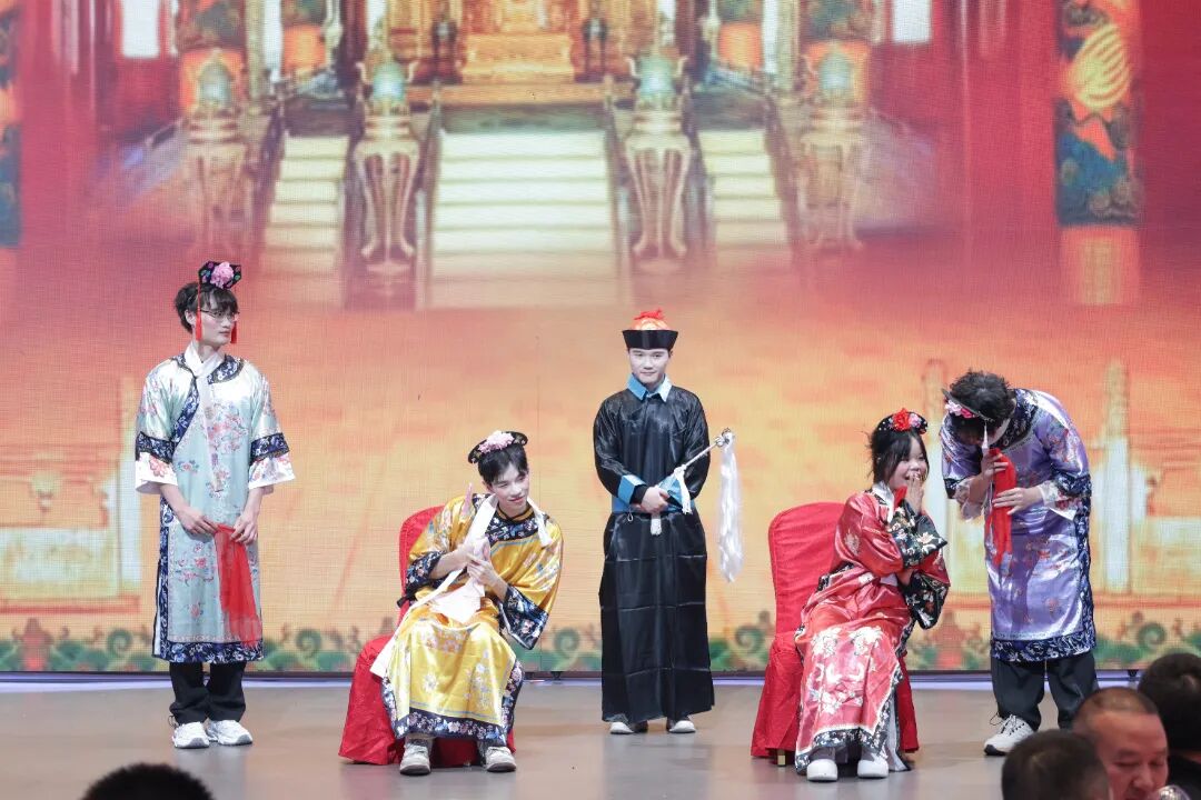 Five performers on stage in Qing dynasty-style costumes with dramatic makeup, set against a backdrop of an ornate palace scene.